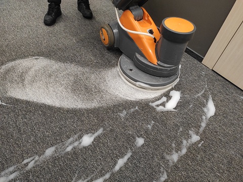 yellow scrubbing machine is using to clean grey carpet