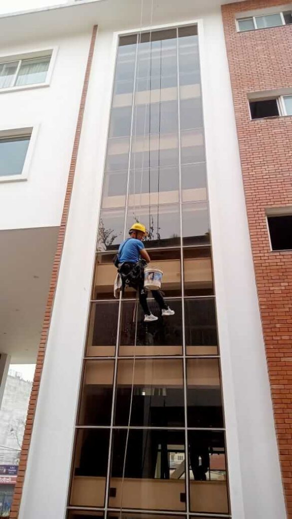 a man cleaning exterior glass by hanging in rope