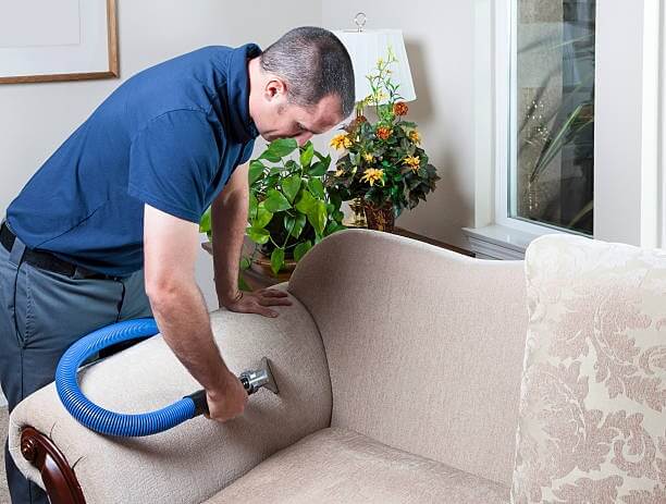 a man vacuuming sofa with vacuum cleaner